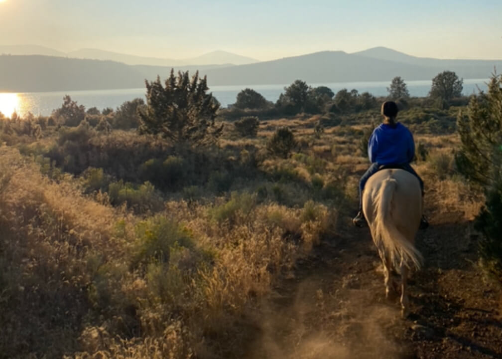 A woman horseback riding on a dirt road.