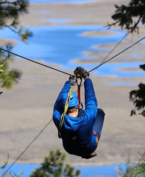 A man wearing blue attire and a matching blue helmet, zip-lining through the trees