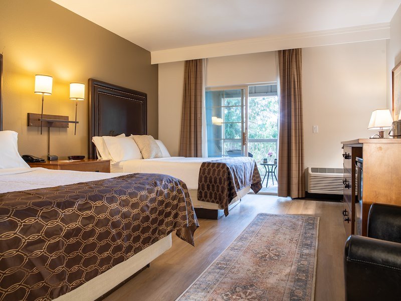 Two queen-sized beds next to each other in a well light room with an open balcony located on one side of the wall.