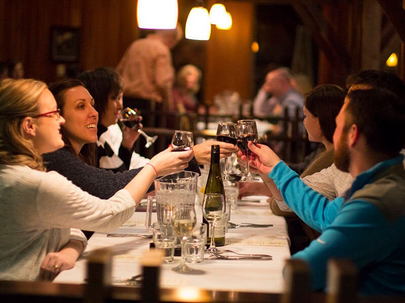 People at a dinner table joyfully raise wine glasses together.