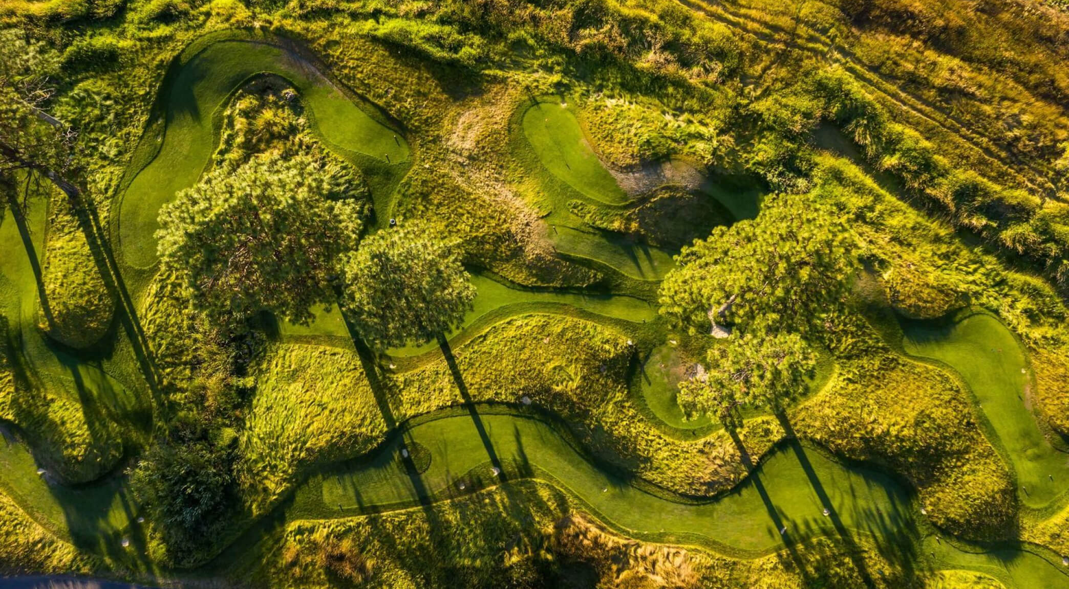 a vibrant mini-golf course with well-maintained greens, colorful obstacles, and scenic surroundings, including trees and a small water feature.