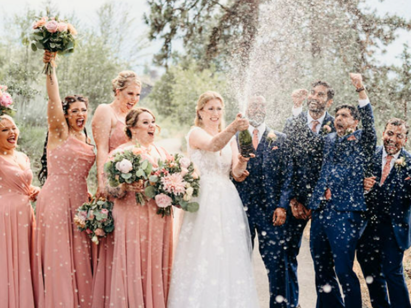 A bride and groom's wedding party, popping a bottle of champagne in celebration.