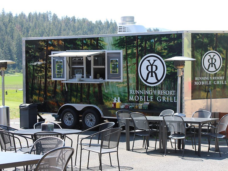 The mobile grill trailer with empty tables and chairs with heating lamps nearby.