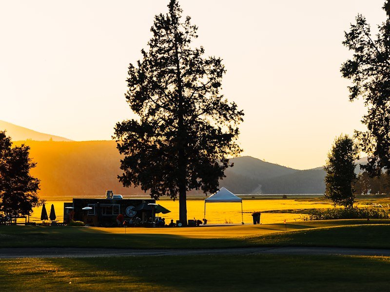 The mobile grill trailer located next to trees at sunset.