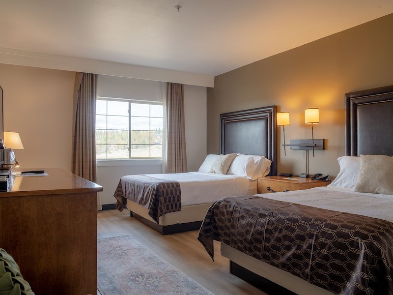 Two queen-sized beds next to each other in a well light room with a large open window located on one side of the wall.