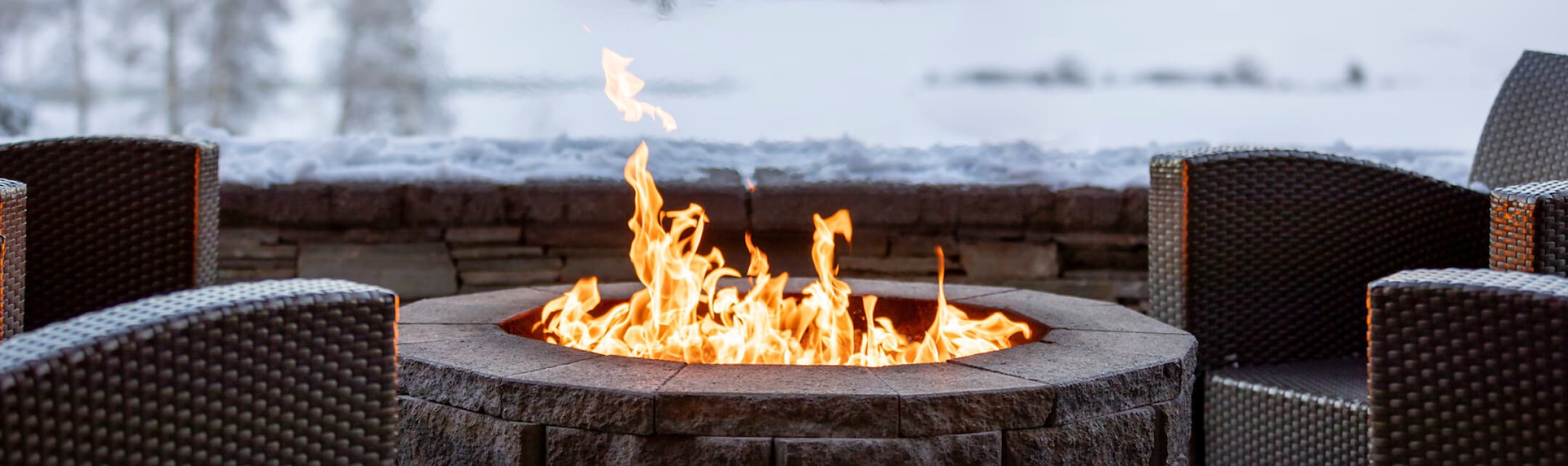 An outdoor patio fire pit with lounge chairs facing towards it.