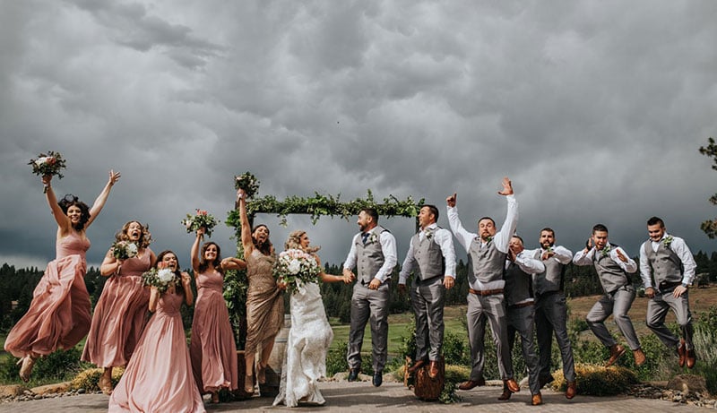 a wedding party joyfully jumping into the air against a backdrop of grey clouds.