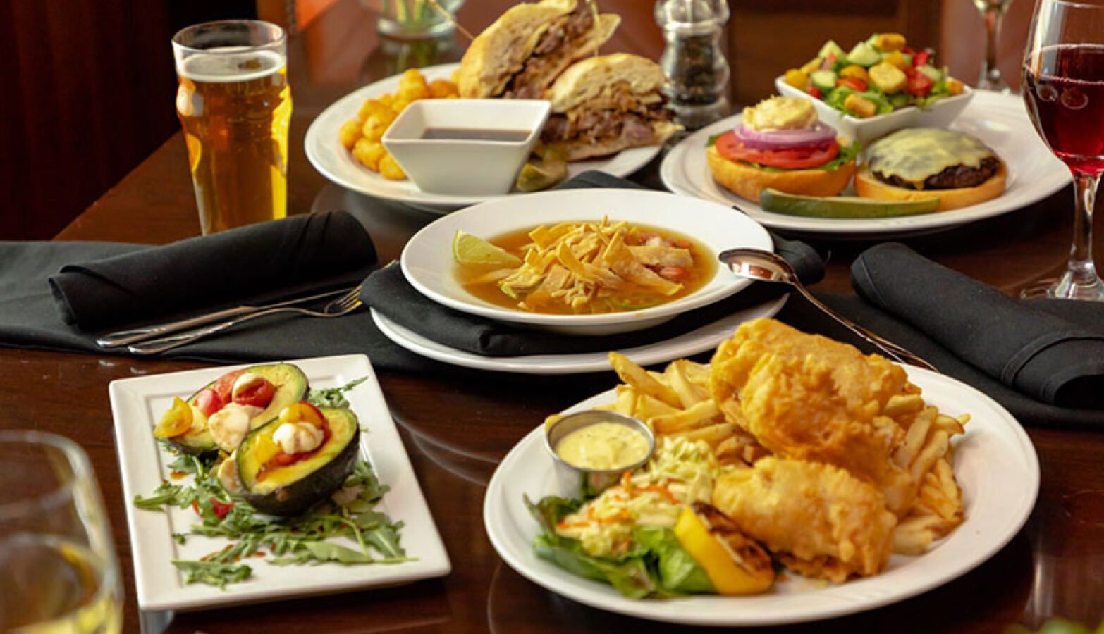 A vibrant spread showcasing crispy fish and chips, a juicy burger, and a stacked sandwich, all presented on elegant plates.