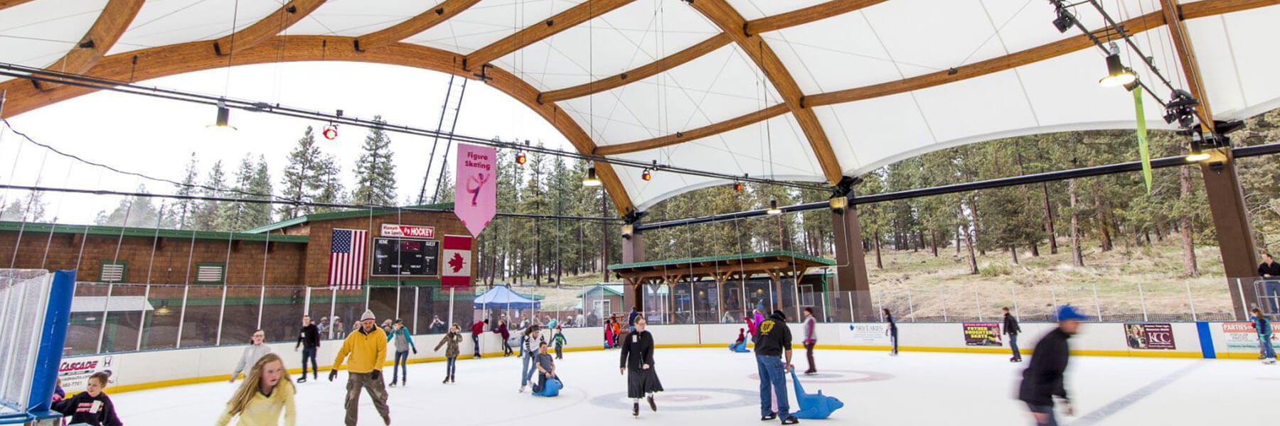 a lively scene of people ice skating at an outdoor rink. The skaters are of various ages.