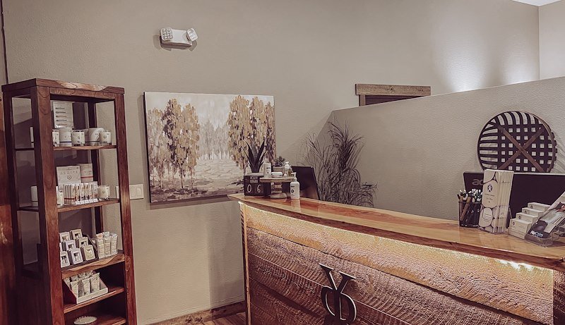 The front desk at the spa, with products stacked on a wooden shelf and a painting of trees on the wall.