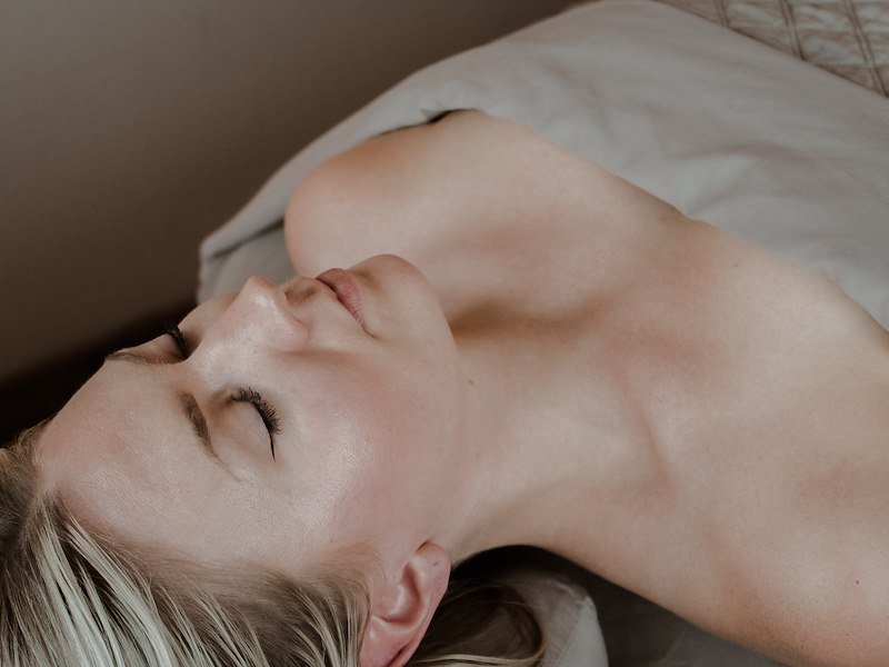 A woman laying down on a table with her eyes closed and with a towel across her body.