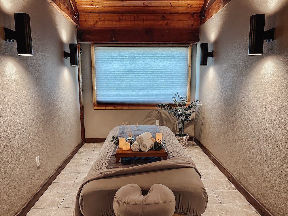 A serene spa room with a massage table centered within it. Four dimly lit lights on the adjacent walls.