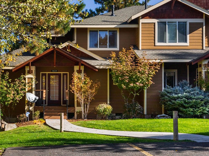 Front view of a brown house, with green grass and a paved walkway leading to the front door.