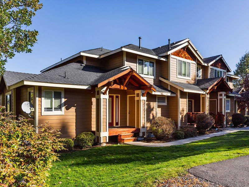 The front view of a vacation home entrance, surrounded by green grass, trees and a paved walkway.