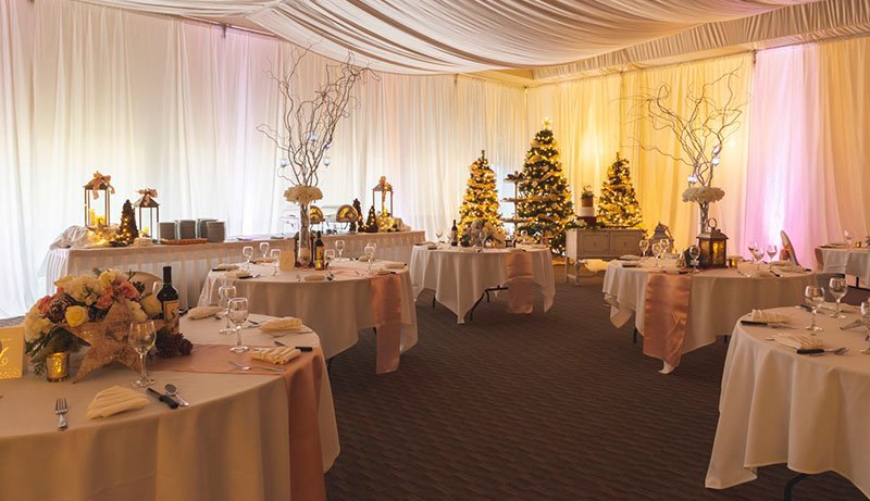 An indoor tent with multiple tables and decorations with colored lighting illuminating against the curtained walls.