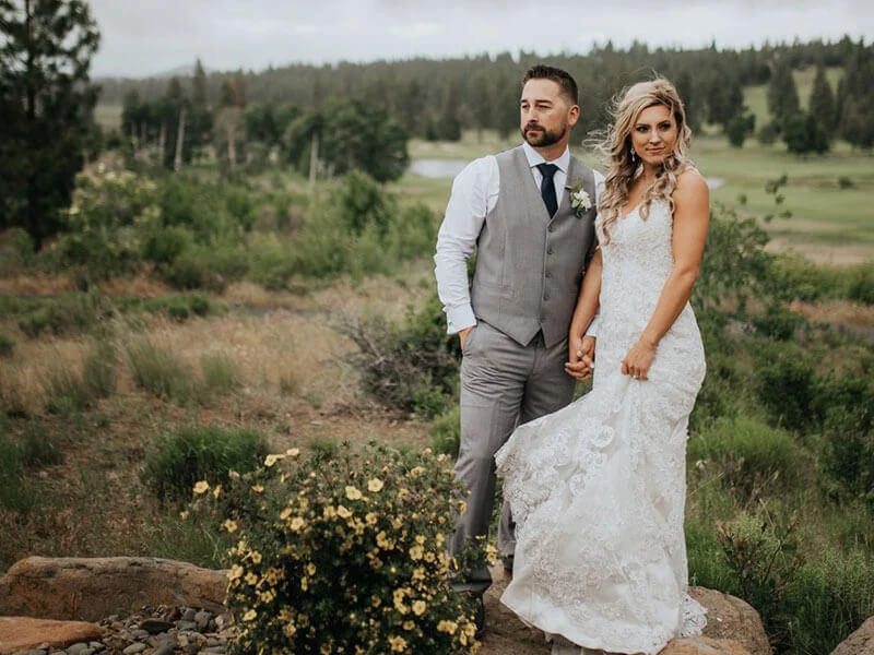 A bride and groom standing on a rock outdoors surrounded by nature.