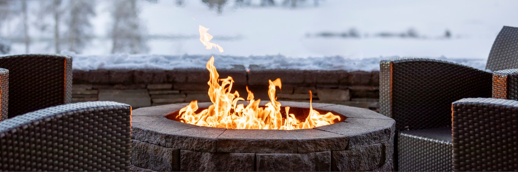 An outdoor patio fire pit with lounge chairs facing towards it.
