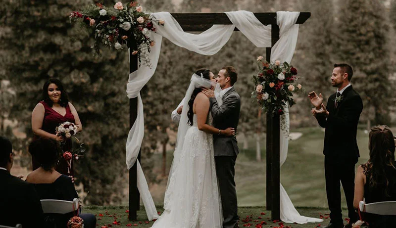 A groom kissing the bride at a wedding alter surrounded by friends and family.