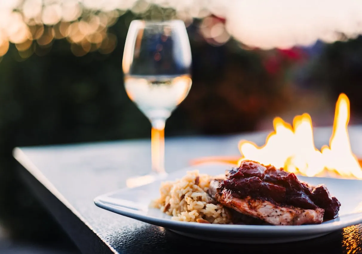A plated dinner and glass of wine beside the fire.