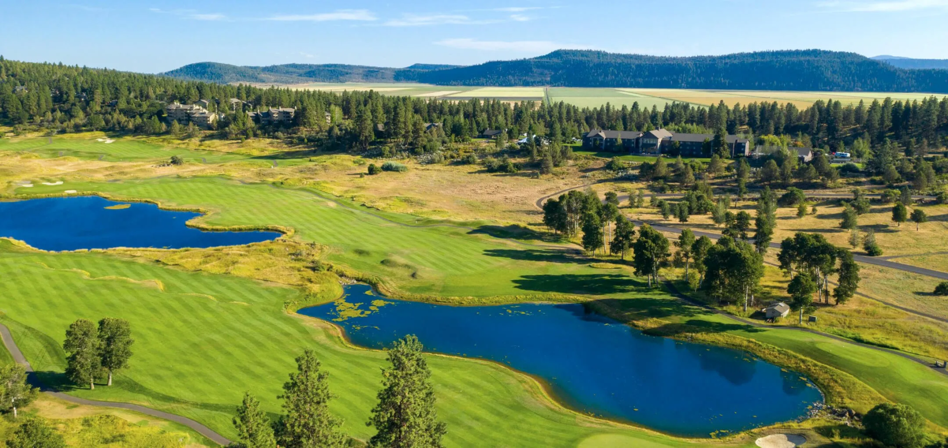 Aerial view of the golf course in the summer, featuring the water features and mountain range in the background.